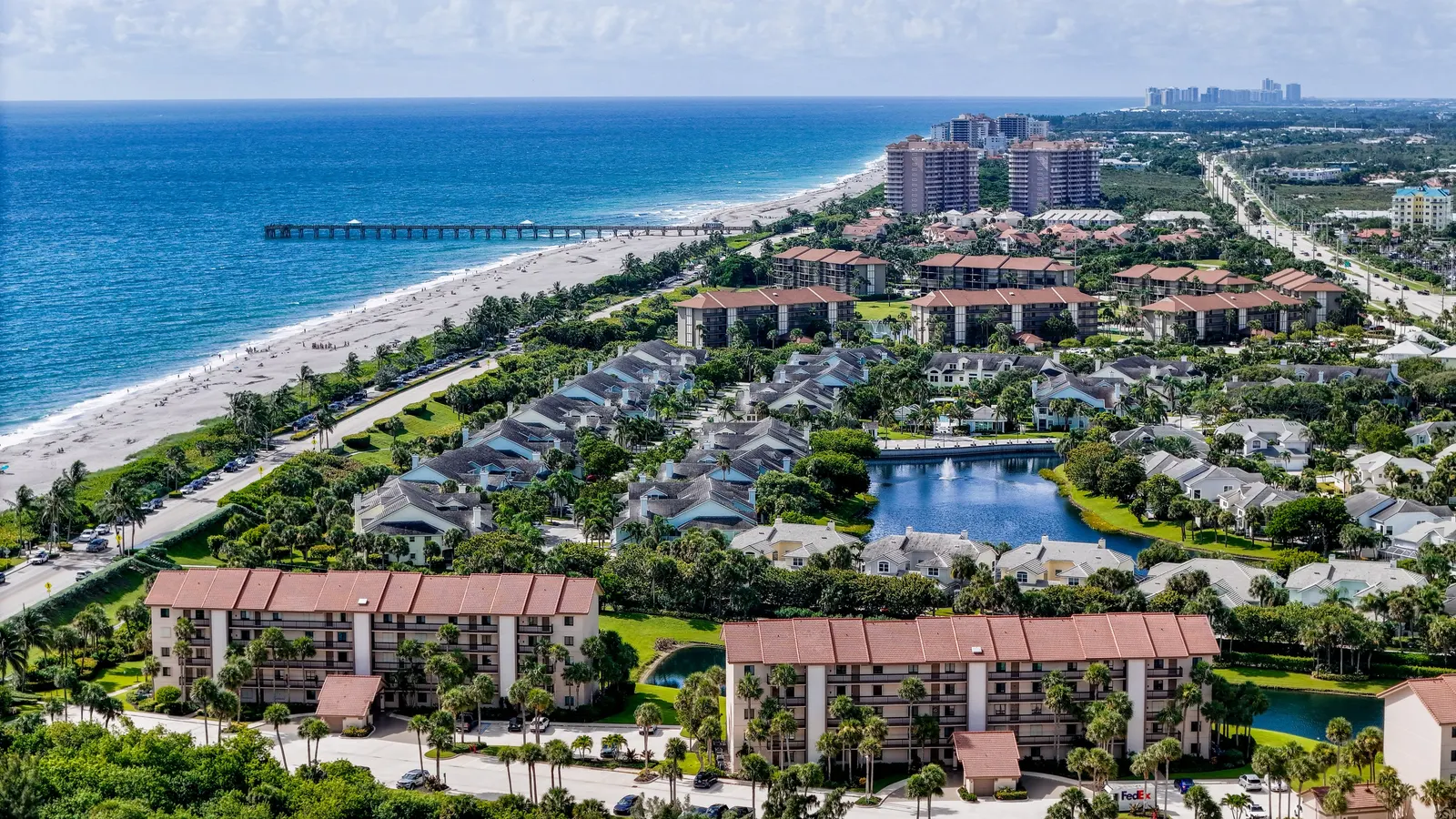 Aerial view of oceanfront condominiums along a Florida beach, with a fishing pier reaching into turquoise Atlantic water